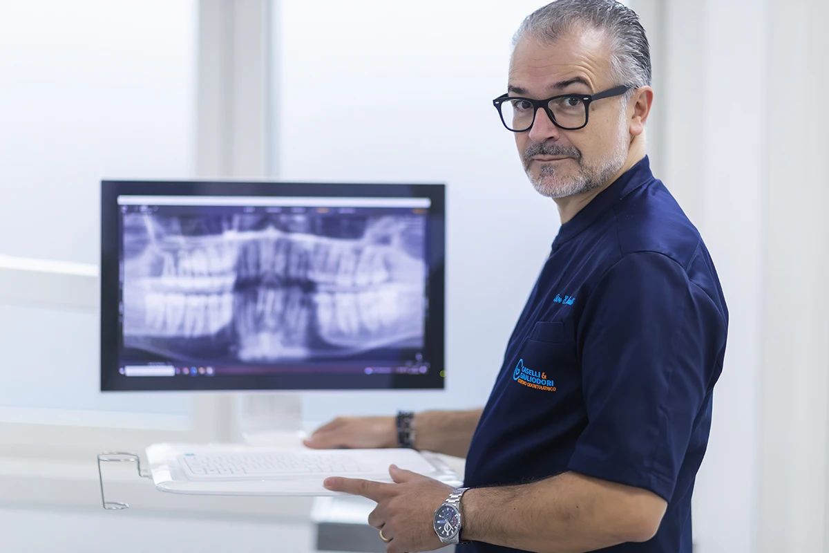 Dottor Caselli osserva 
                una radiografia dentale su uno schermo del computer in uno studio odontoiatrico moderno 
                e luminoso. L ambiente trasmette professionalità e attenzione al paziente.